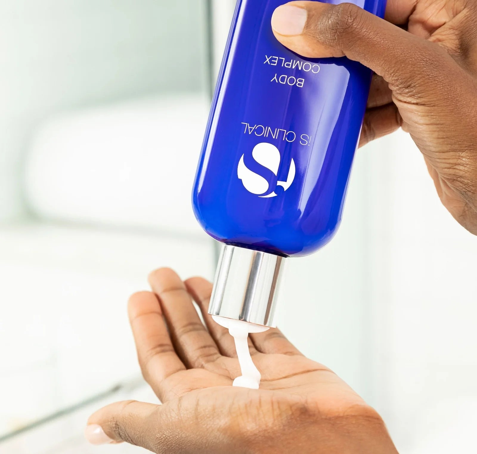 Hand holding a blue bottle with a pump, dispensing a white substance onto another hand.