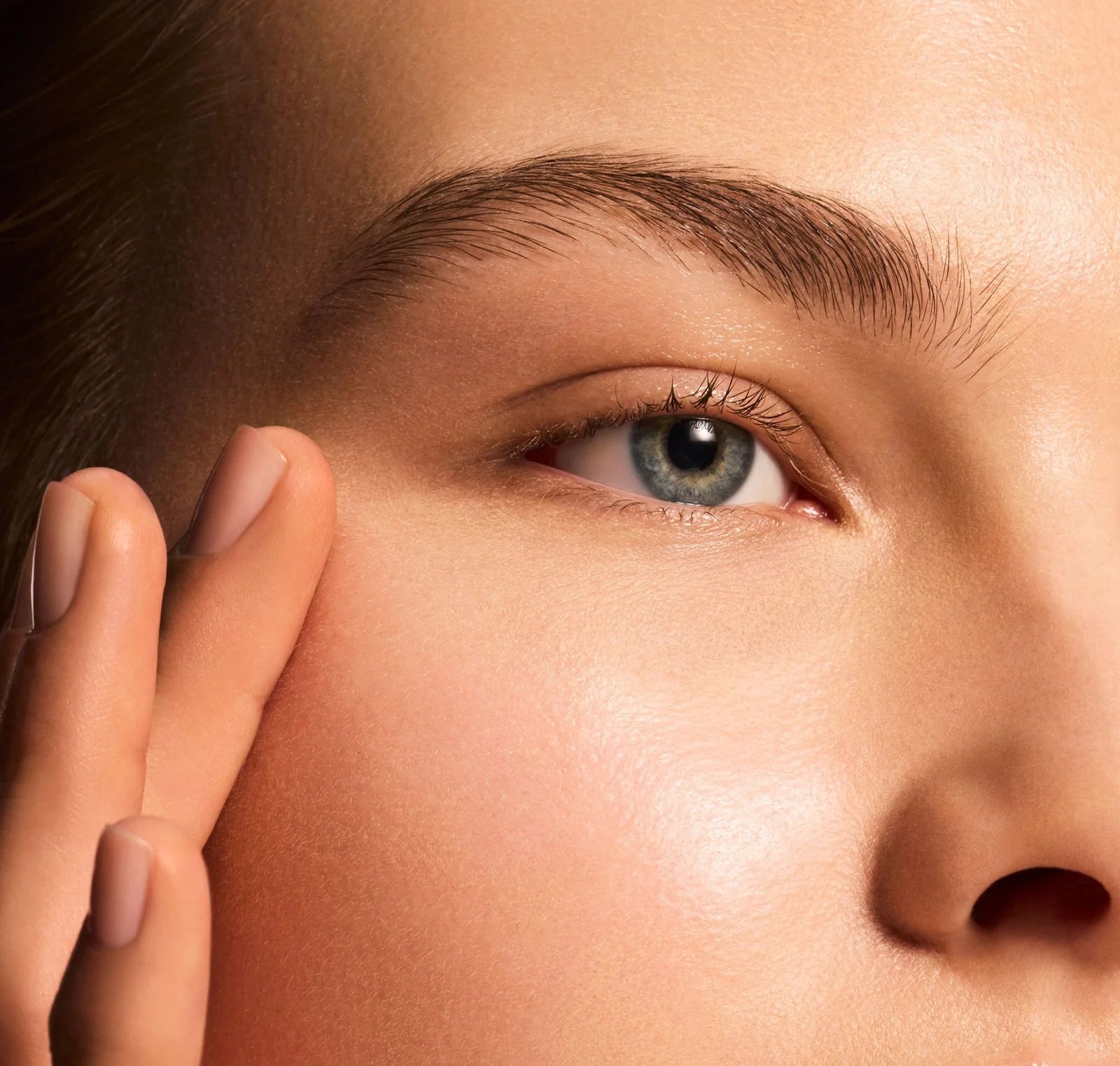 Close-up of a person's eye with a hand gently touching the skin around it.