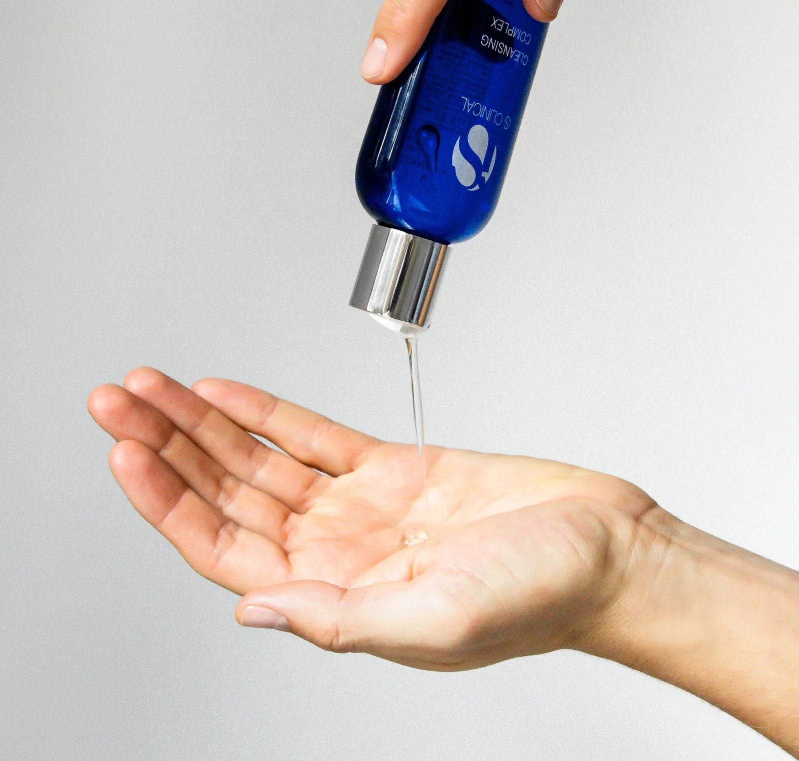 Blue bottle with a dropper being used to dispense liquid onto a hand against a gray background