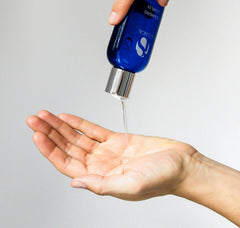 Blue bottle with a dropper being used to dispense liquid onto a hand against a gray background