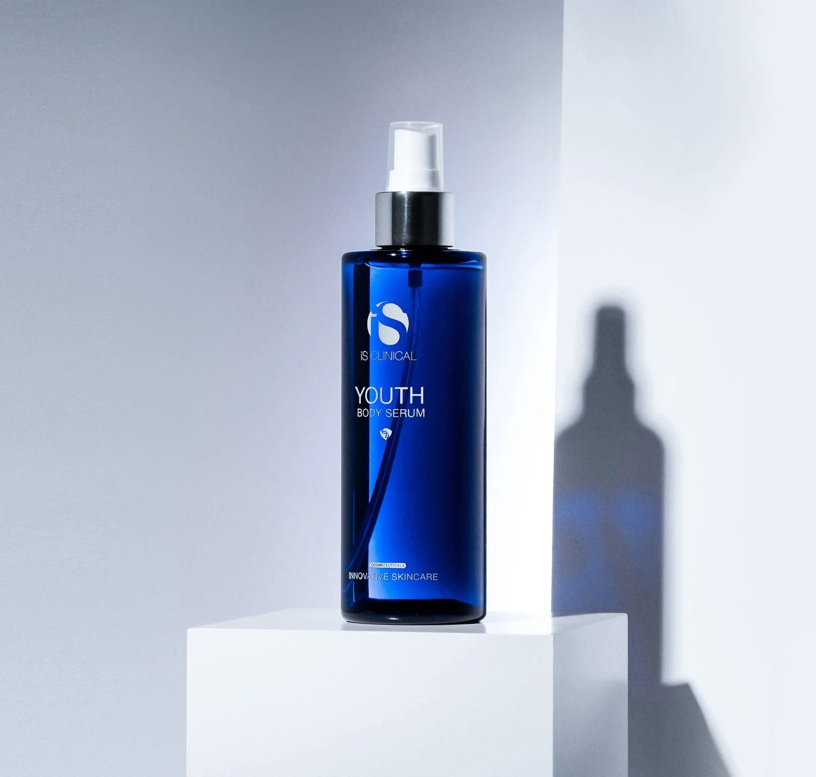 Blue serum bottle with spray mechanism on a white platform against a gray background