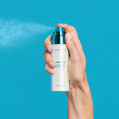 Hand holding a bottle of hair serum with a blue background