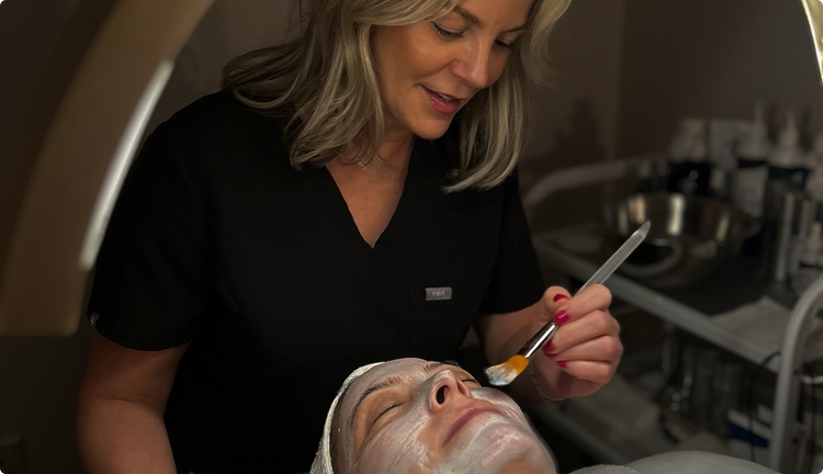 Person applying a facial mask to another person in a clinical setting.