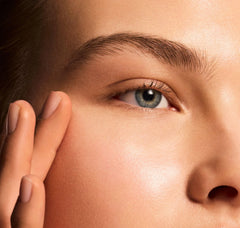 Close-up of a person's eye with a hand gently touching the skin around it.