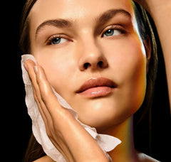 Woman cleaning her face with a white cloth against a black background
