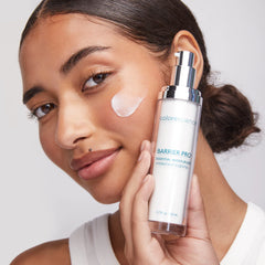 Woman holding a skincare product with a visible brand name on a neutral background