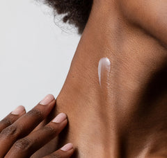 Close-up of a hand applying cream to a shoulder with a neutral background
