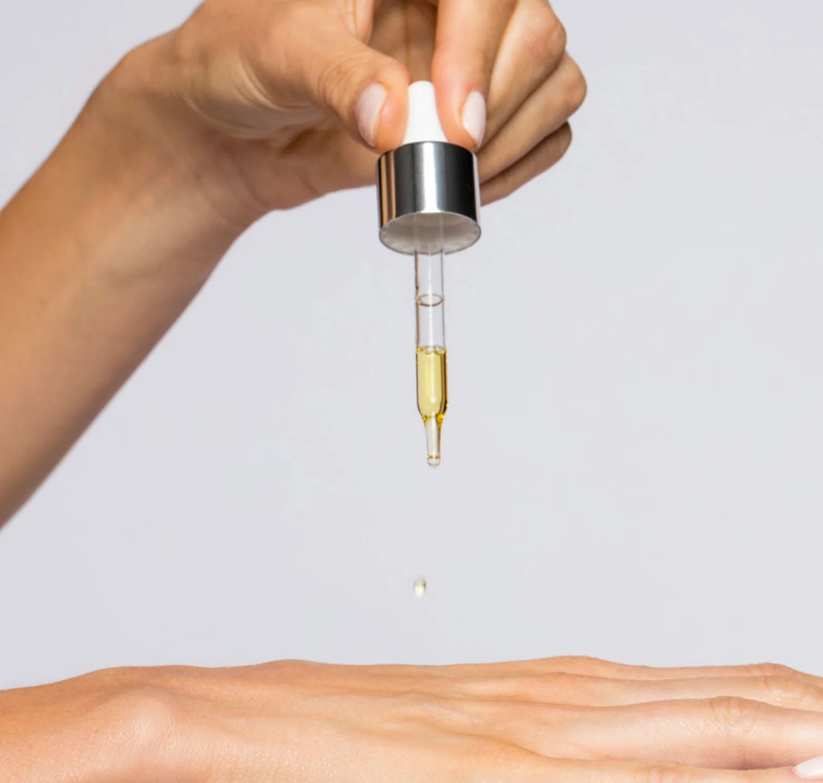 Hand holding a dropper with a clear liquid above skin