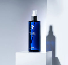 Blue serum bottle with spray mechanism on a white platform against a gray background